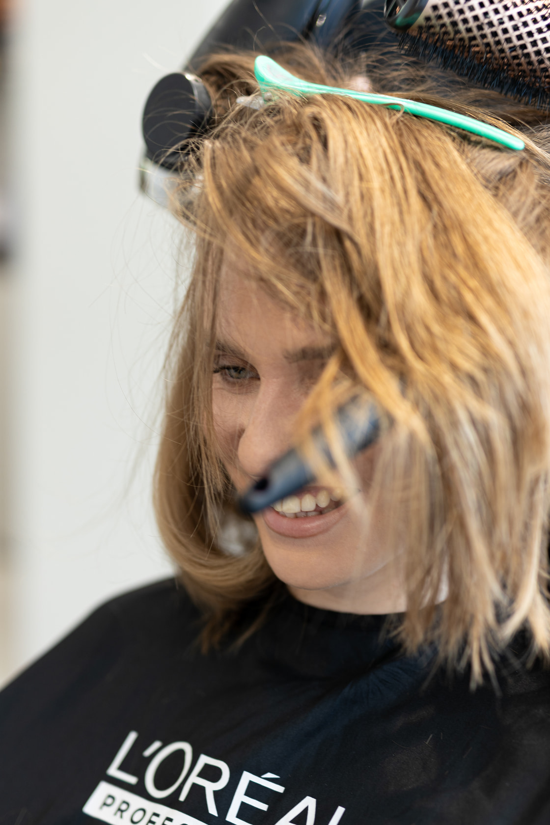 Client smiling mid-blow-dry, hair lifted by the round brush