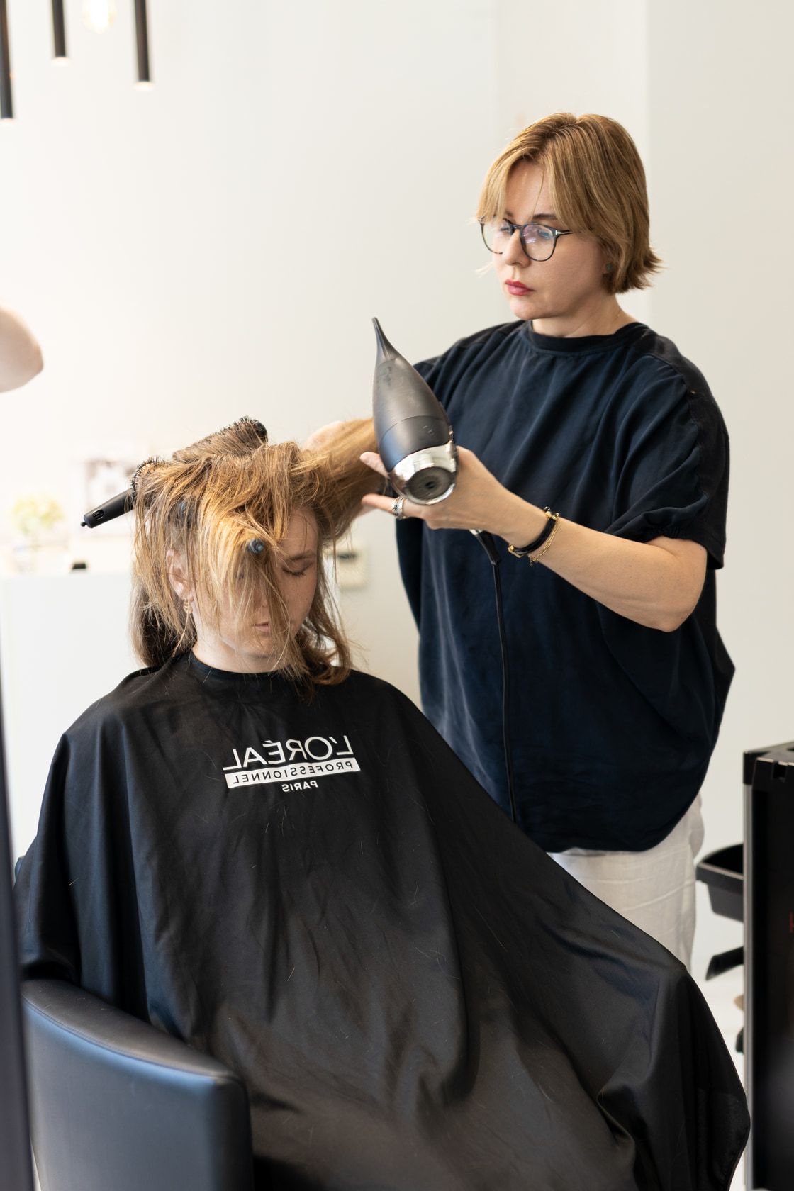 Stylist blow-drying a client’s hair from behind the chair